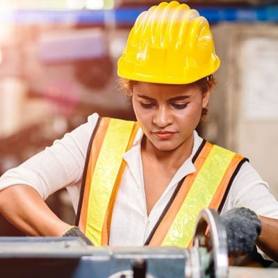 Photo of a woman wearing a work vest and hardhat working machinery 