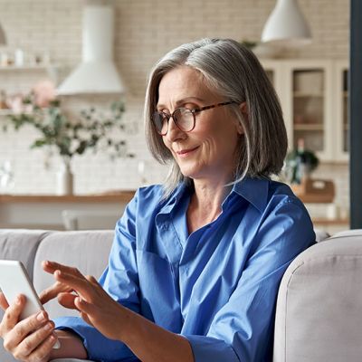 Photo of a woman sitting on a couch smiling at her phone