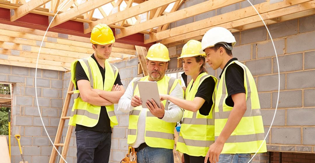 Photo of a team of four workers wearing hard hats and work vests looking at a clipboard