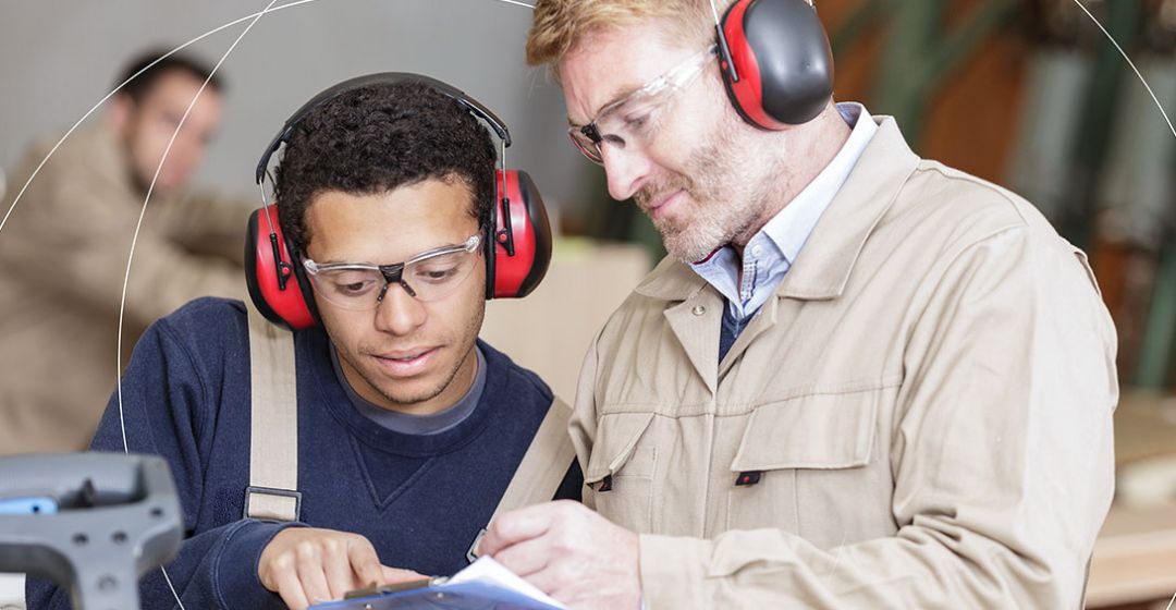 Photo of two men wearing earmuffs looking at a clipboard